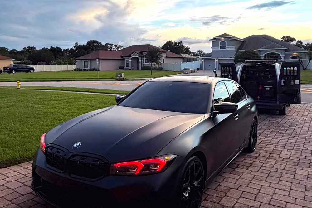 A matte black BMW at sunset with the GaliGloss van behind it